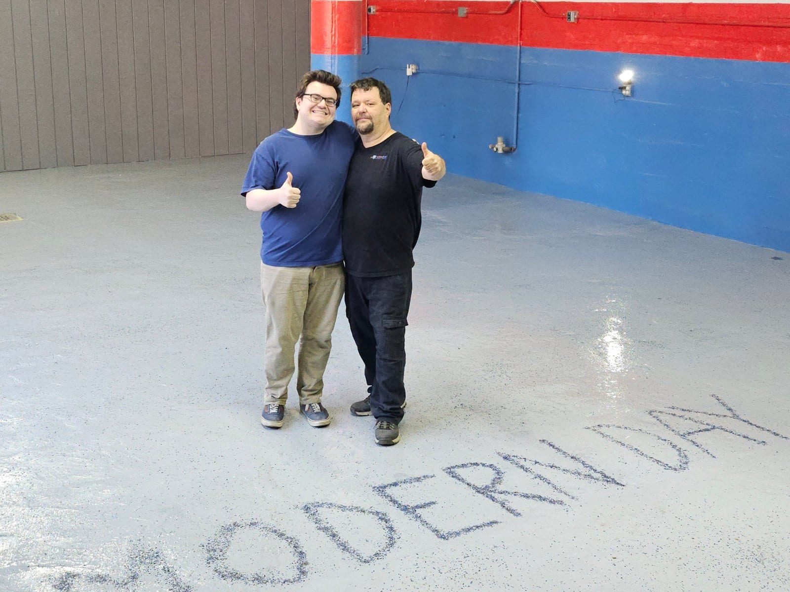 Two of the Modern Day Muffler & Brakes team giving a thumbs-up on the shop floor, with MODERN DAY written on the floor